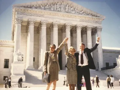 Photo of three adults standing in front of a government building